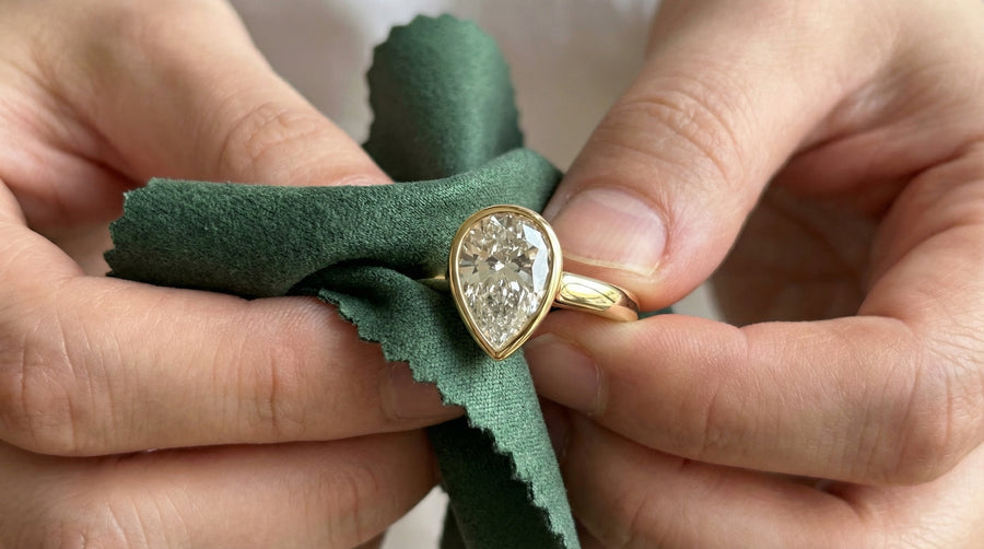 Hands polishing a pear-shaped diamond ring with a green cloth