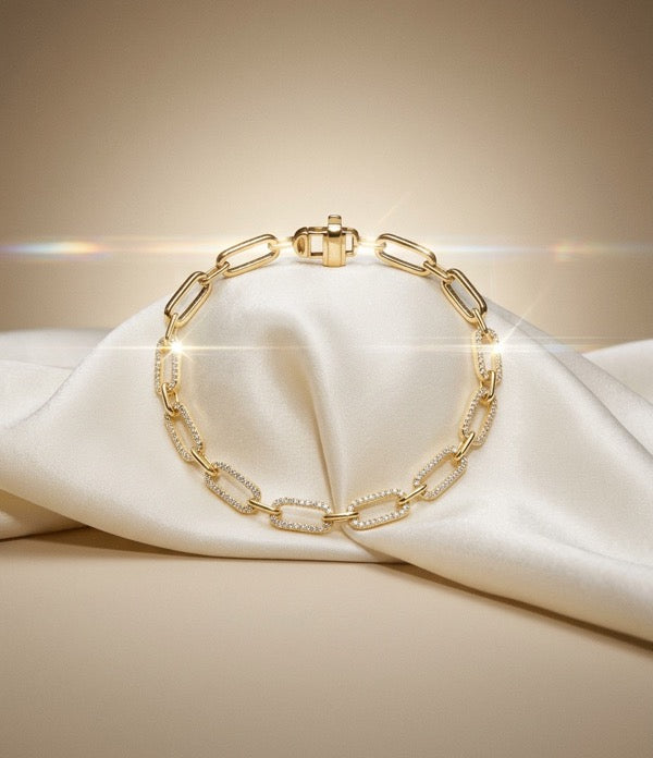 A yellow gold paperclip link bracelet set with pavé diamonds, on ivory satin.