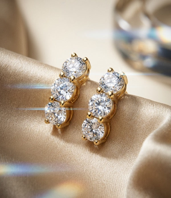 Three-stone round diamond drop earrings in yellow gold on champagne satin.