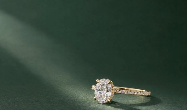 An oval diamond engagement ring with a hidden halo and pave band in yellow gold, resting on deep green paper in soft window light.