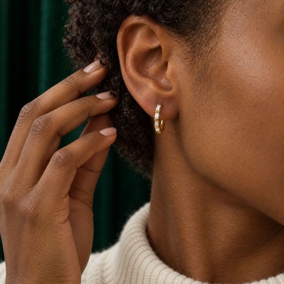 Close-up of a woman tucking a curl behind her ear, wearing a small gold huggie set with four baguette diamonds.