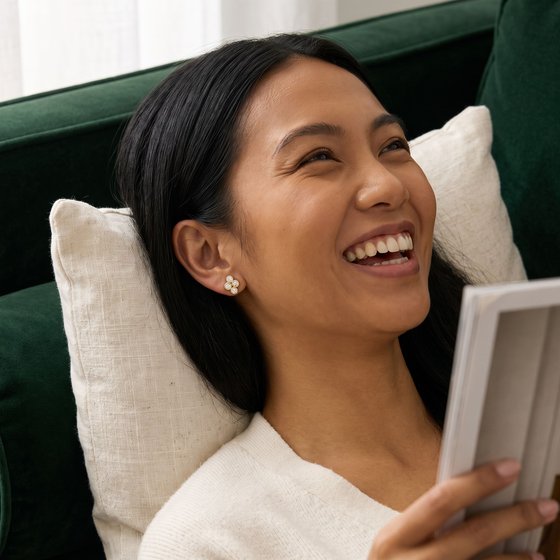 A woman laughing on a green velvet sofa, wearing a quad cluster stud of four bezel-set diamonds.