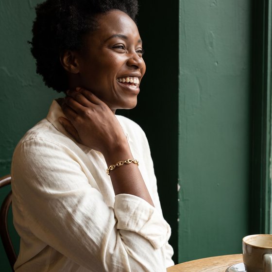 A woman laughing in a cafe, her hand at her collarbone showing a gold mariner link bracelet set with small diamonds.