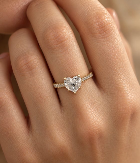 Heart-shaped diamond in claw prongs on a yellow gold band set with small pavé diamonds.
