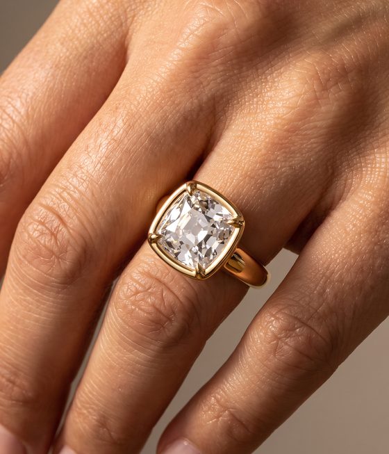 Old mine cushion-cut diamond in a yellow gold bezel with claw tips on a wide band.