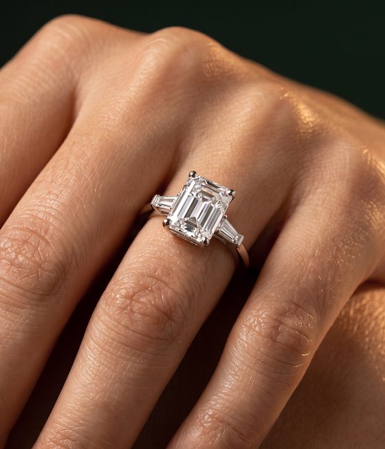 Emerald-cut diamond set north-south with a tapered baguette diamond on each side, on a slim polished band.