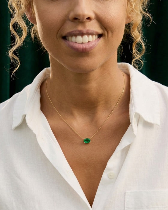 The open collar of a white linen shirt with a small emerald solitaire pendant on a fine gold chain.