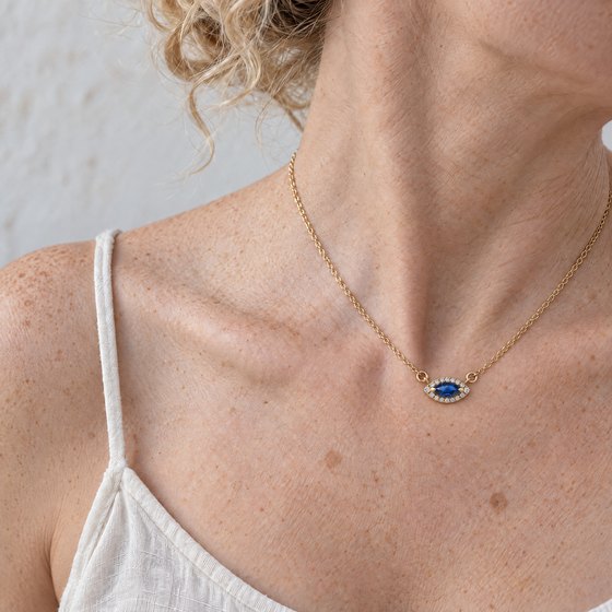 The side of a woman's neck and collarbone wearing a marquise blue sapphire and diamond pendant on a fine gold chain.
