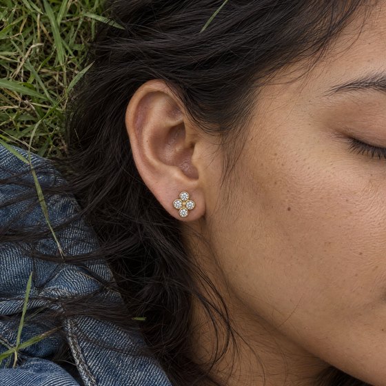 A woman lying in the grass with her eyes closed, wearing a quad stud of four small diamonds.