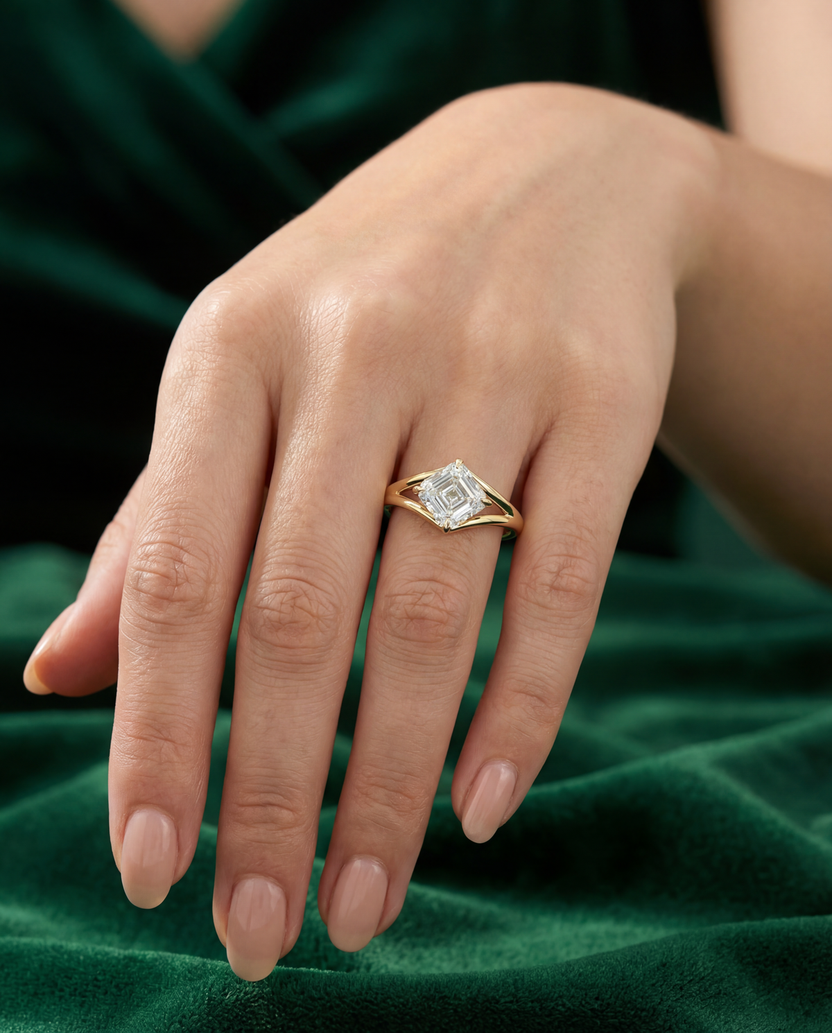 A hand on green velvet wearing a yellow gold ring with an Asscher-cut diamond