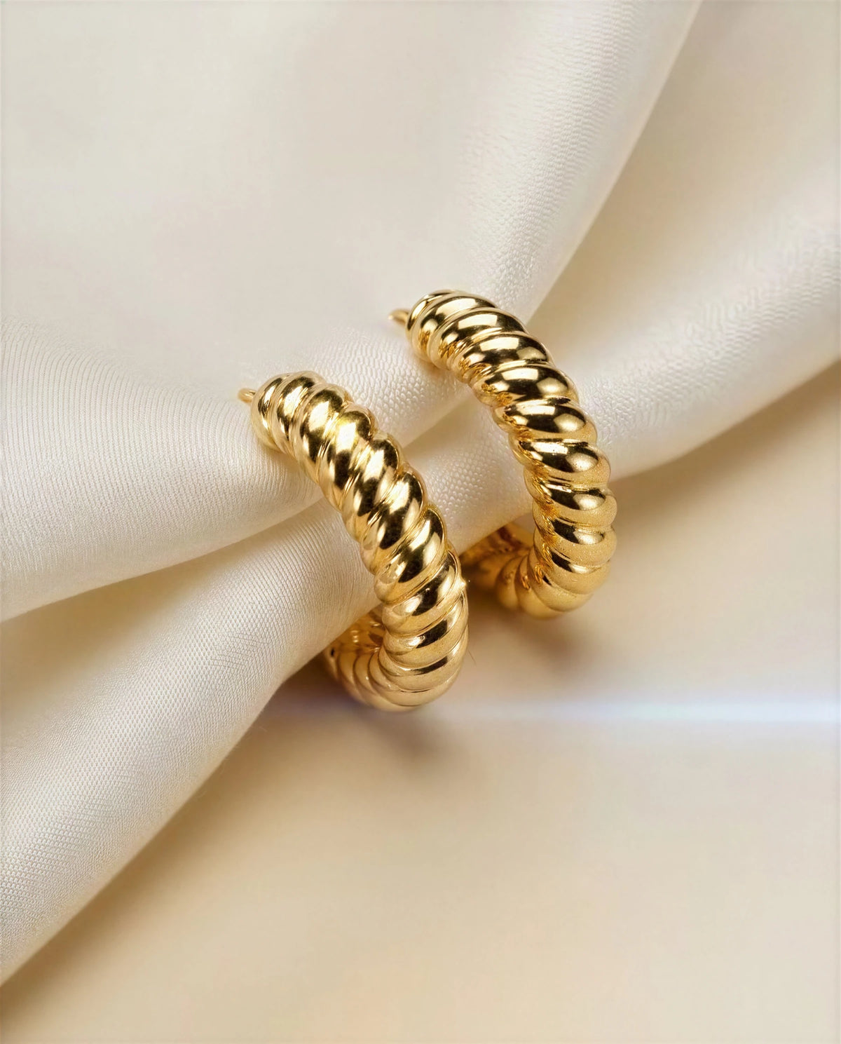 Marigold 14k gold ribbed croissant hoops on ivory satin, a third angle