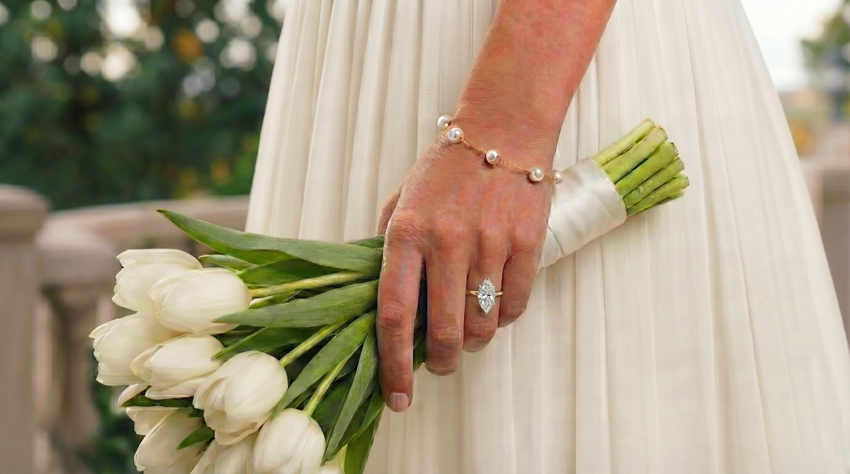 A woman in a white dress holding white tulips, wearing a marquise diamond ring and a pearl bracelet