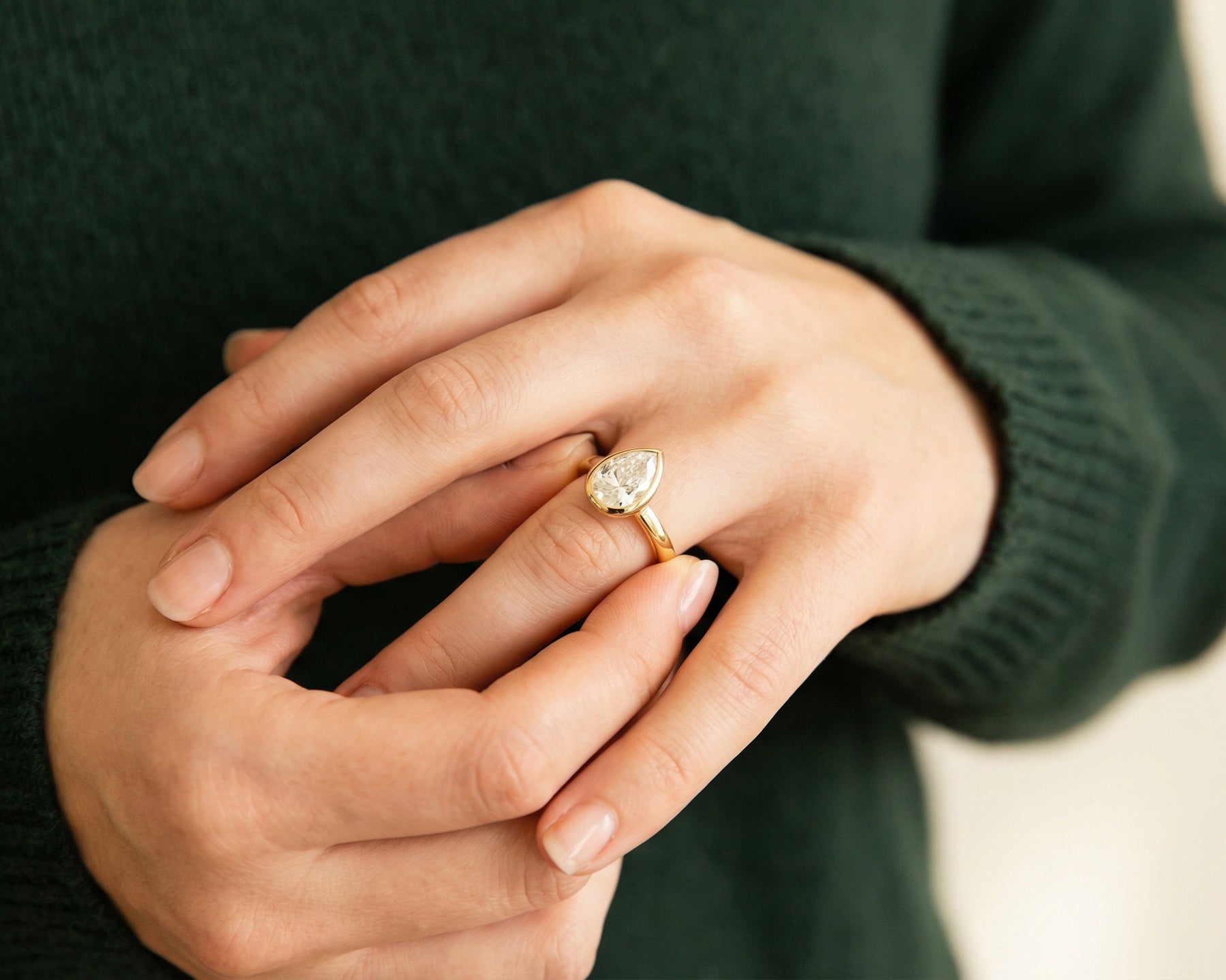 A pear-shaped diamond engagement ring in yellow gold on a woman's hand