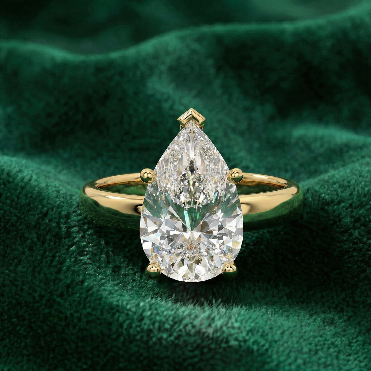 Luna pear solitaire engagement ring in yellow gold on green velvet