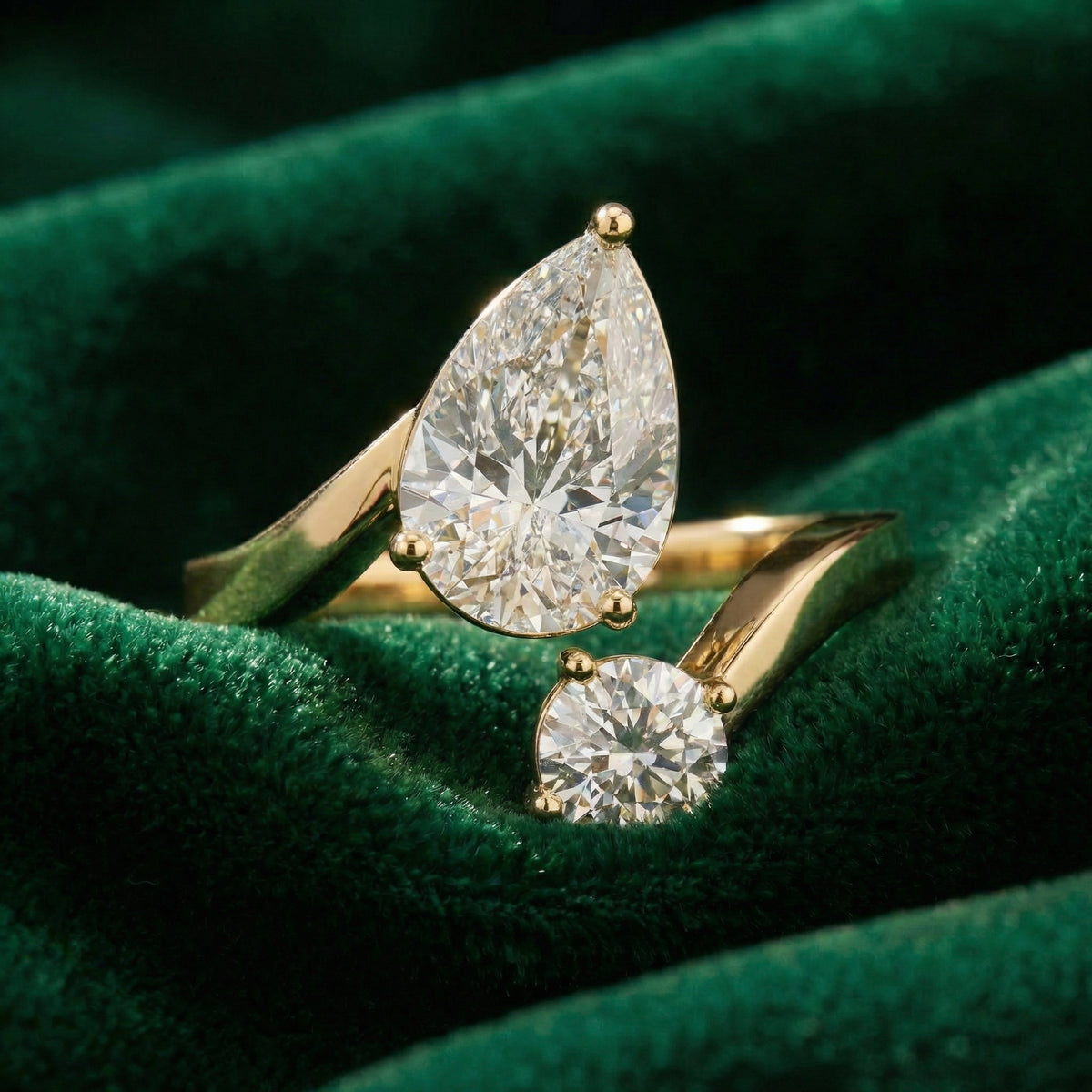 A yellow gold toi et moi ring with a large pear diamond and a round diamond on green velvet