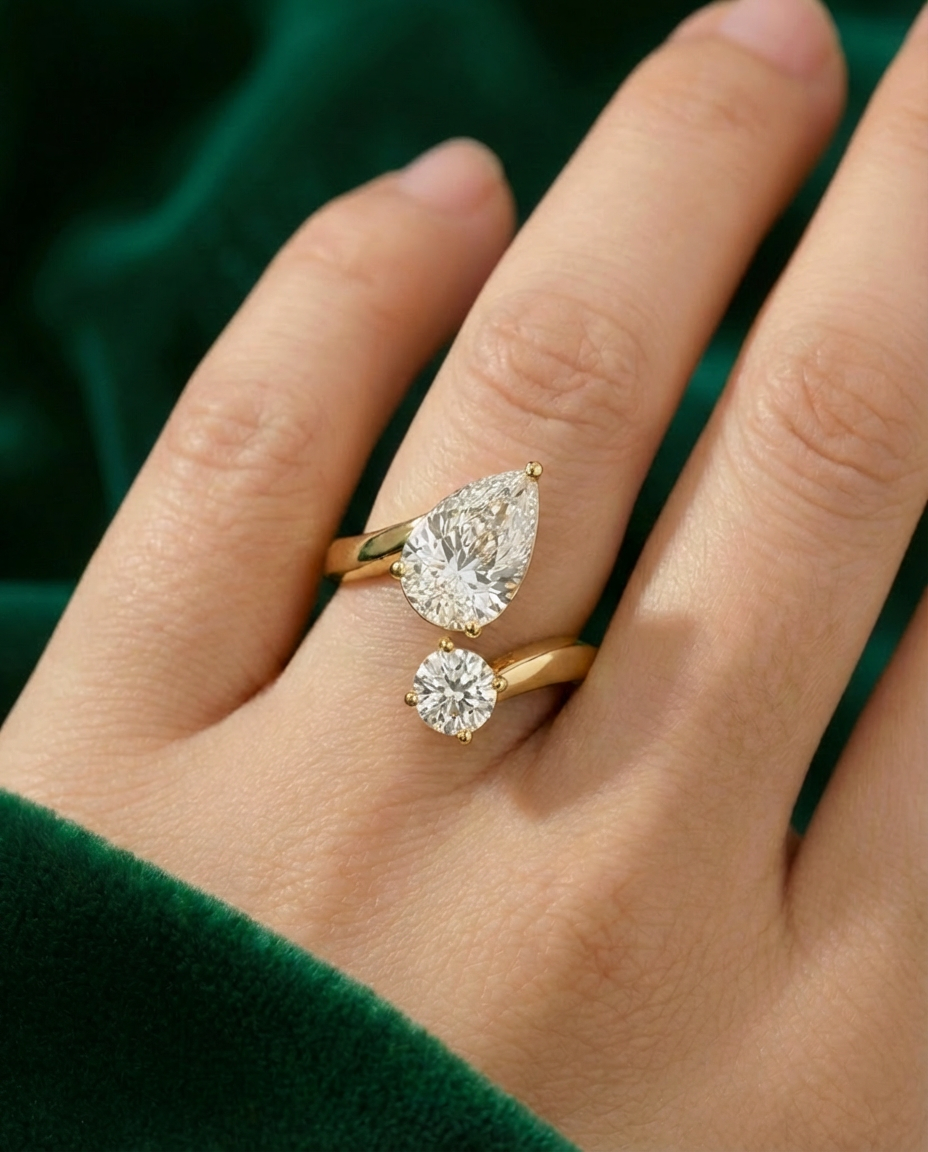 A hand wearing a yellow gold toi et moi ring with a pear diamond and a round diamond