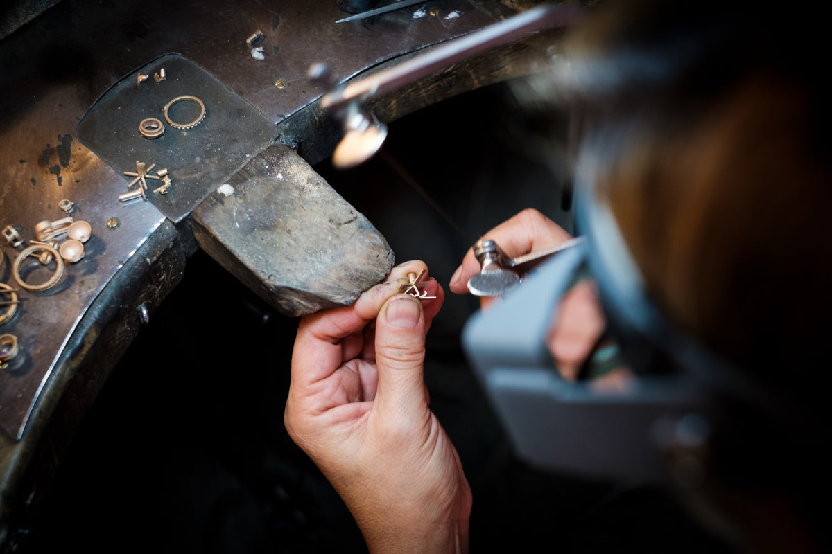 A jeweler working on a ring at the bench pin, with rings and tools on the workbench
