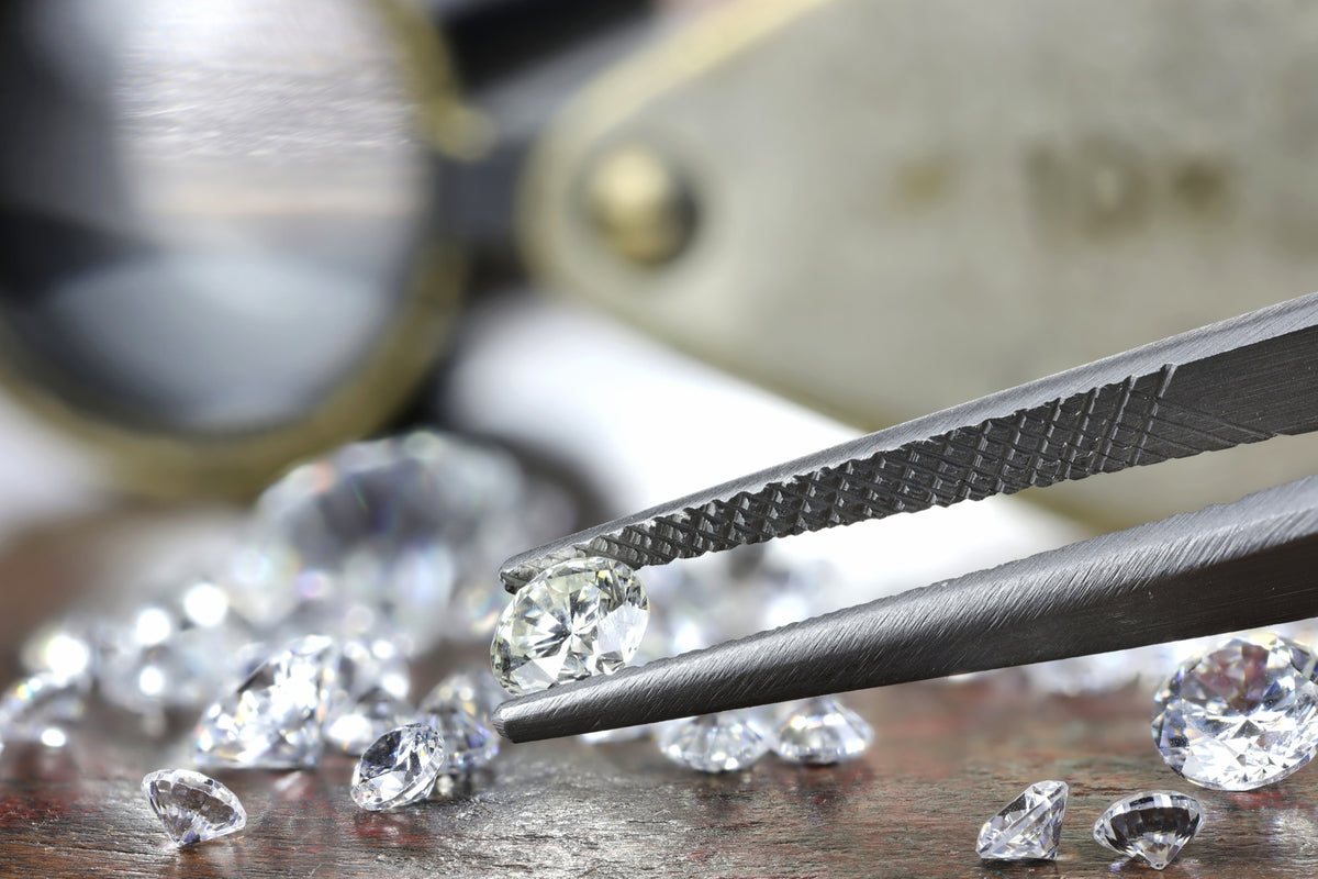 Loose round diamonds on a workbench, one held in steel tweezers