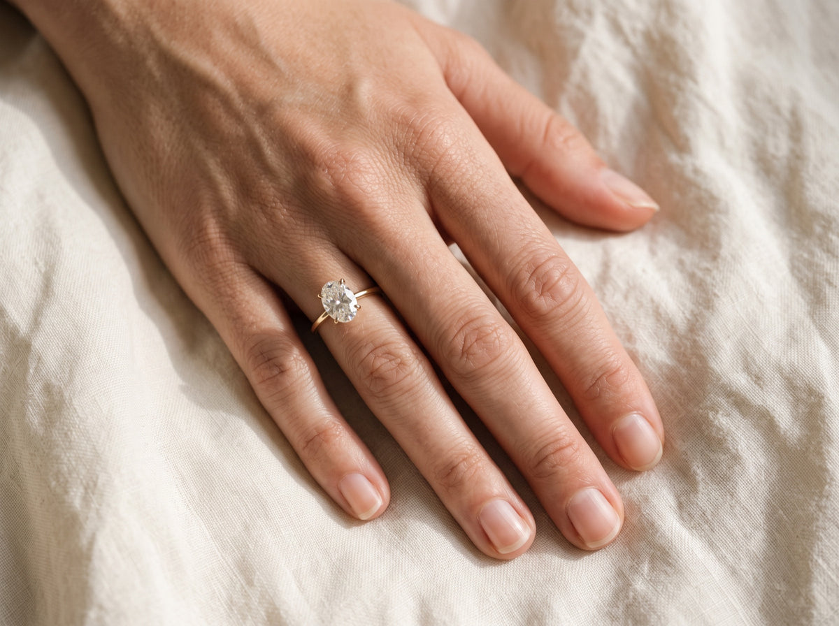 An oval diamond solitaire engagement ring worn on the ring finger of the right hand