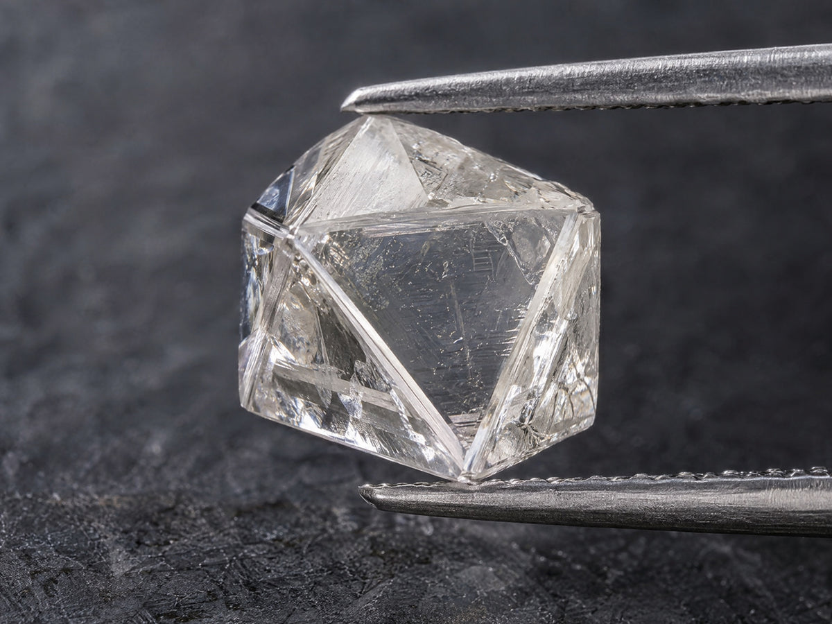 A rough diamond crystal held in steel tweezers above dark slate