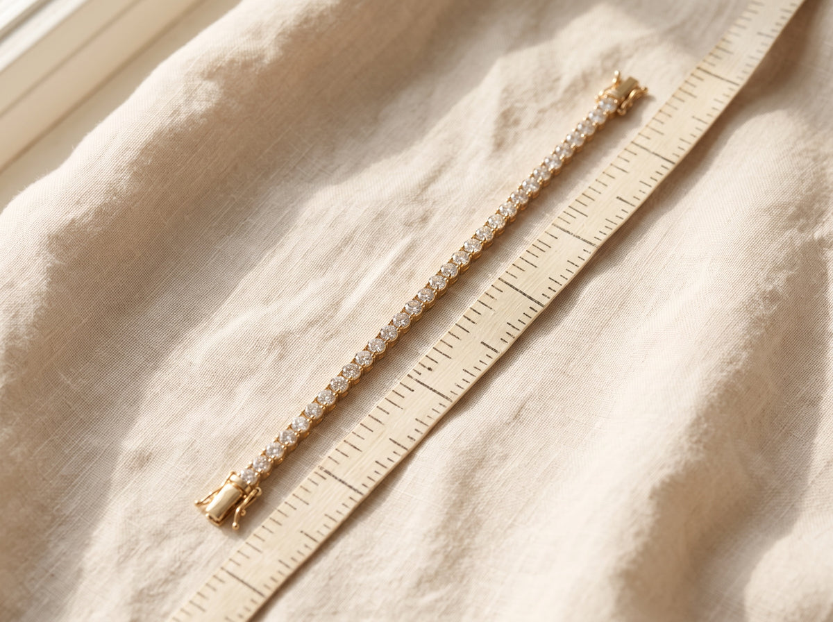 A yellow gold diamond tennis bracelet laid beside a tailor's measuring tape