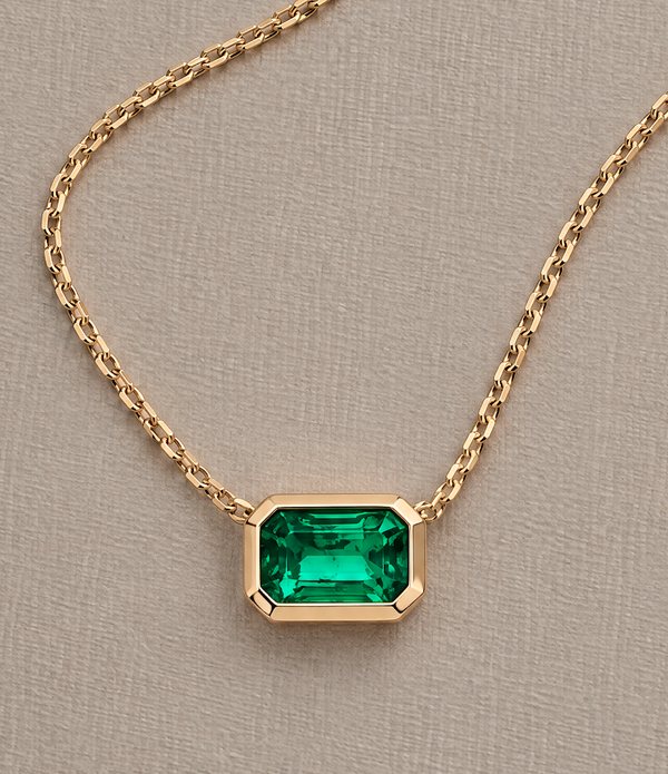 A green emerald-cut stone in a gold bezel pendant on a fine gold cable chain.