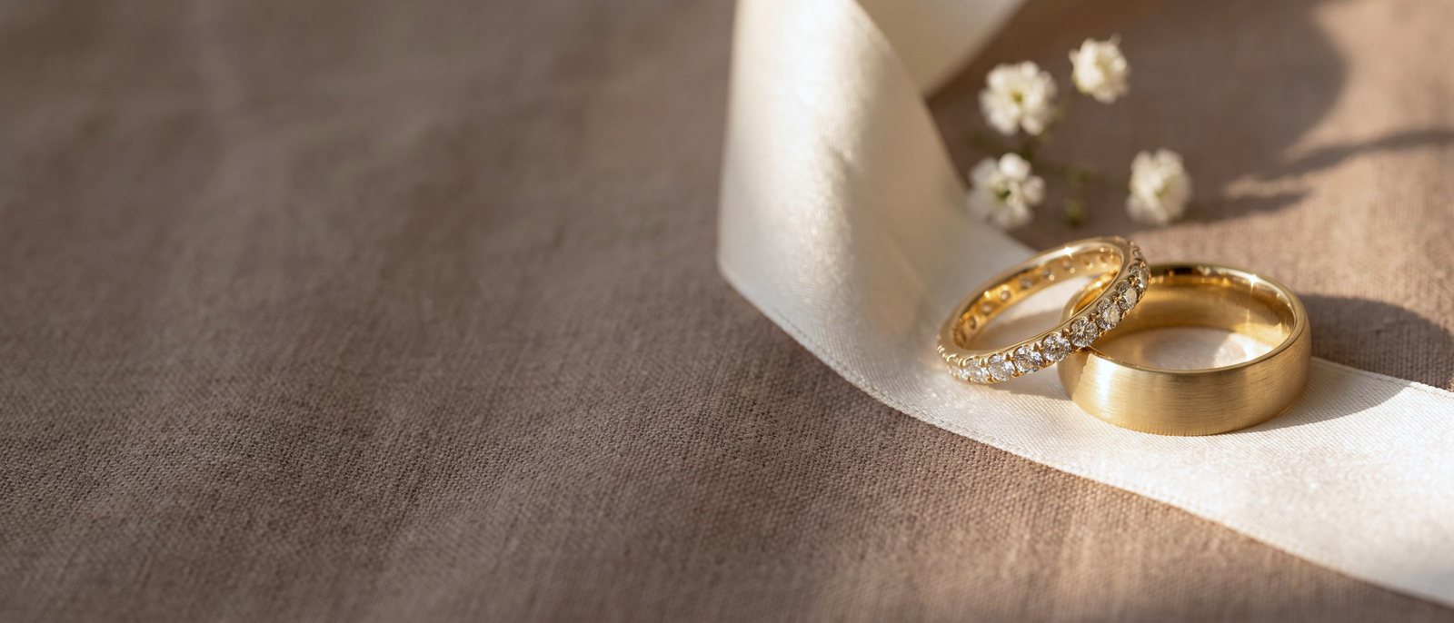 A diamond eternity band and a brushed gold wedding band resting together on ivory silk ribbon.