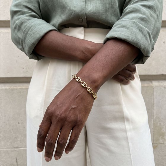 Arms folded at the waist in a sage linen shirt, wearing a gold mariner link bracelet set with small diamonds.