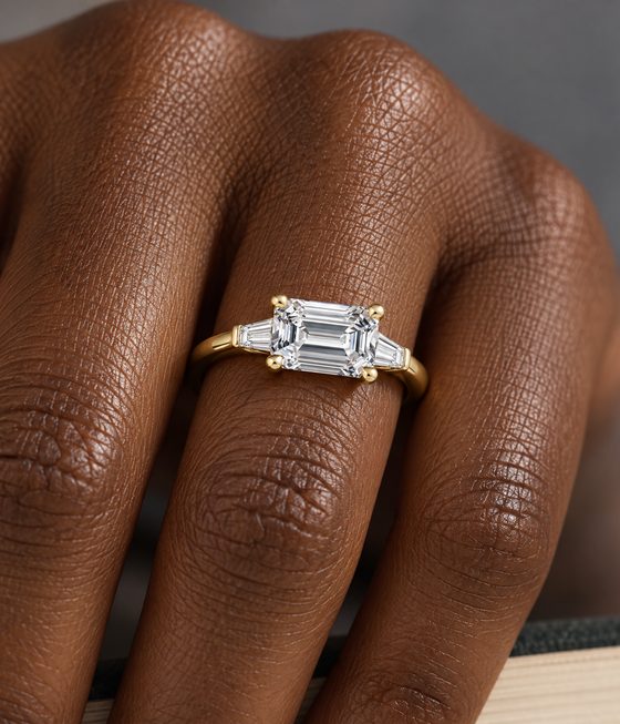 Emerald-cut diamond set east-west between two tapered baguette diamonds on a yellow gold band.