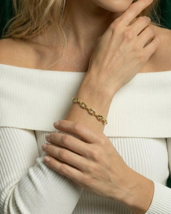 A wrist in a white off-the-shoulder knit wearing a gold link bracelet set with diamonds.